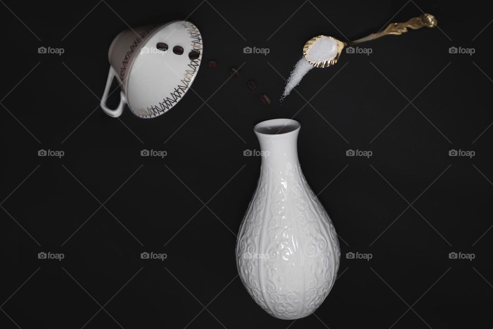 Coffee grains and sugar from a golden spoon are poured into a white vase. Creative still life.