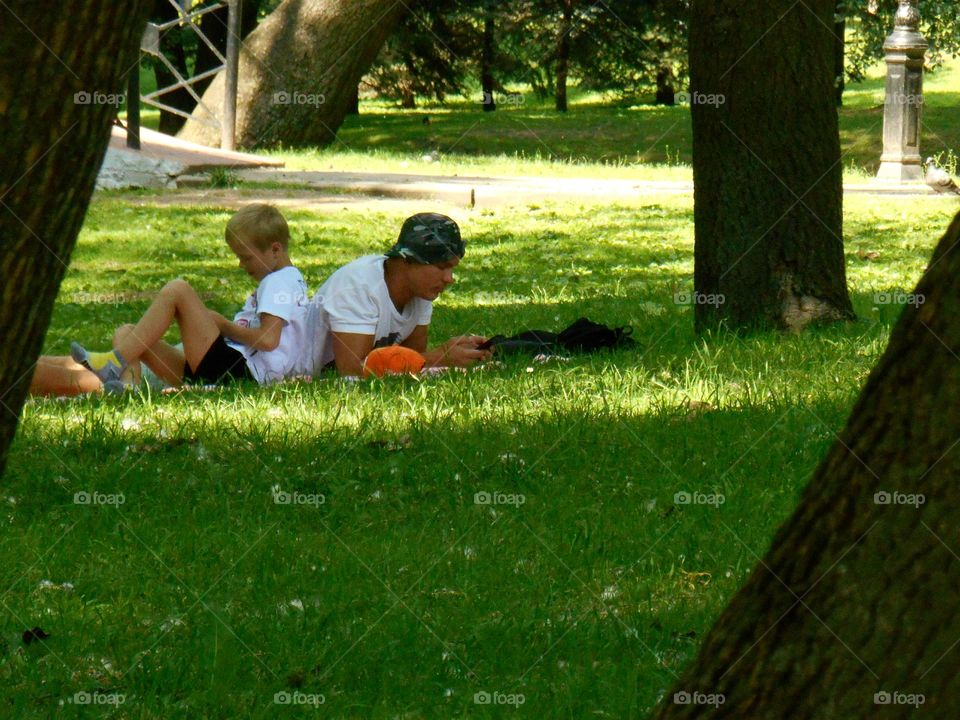 Father and son rest in the park on the green grass