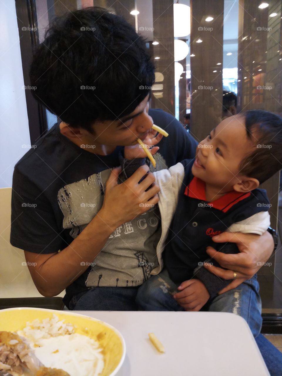 father and son moment in a fastfood chain. The son is so happy while the father is doing funny faces