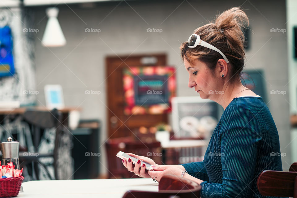 Young woman using mobile phone sitting by a table in cafe