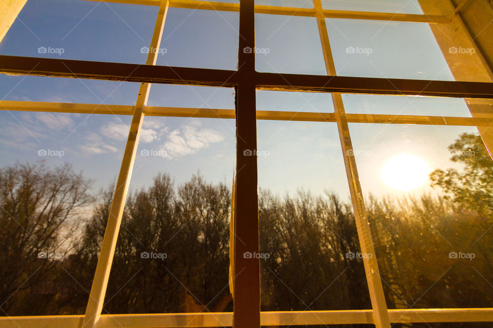 Window at sunset with rectangle and square shaped steel frames with sun trees and blue skies outside