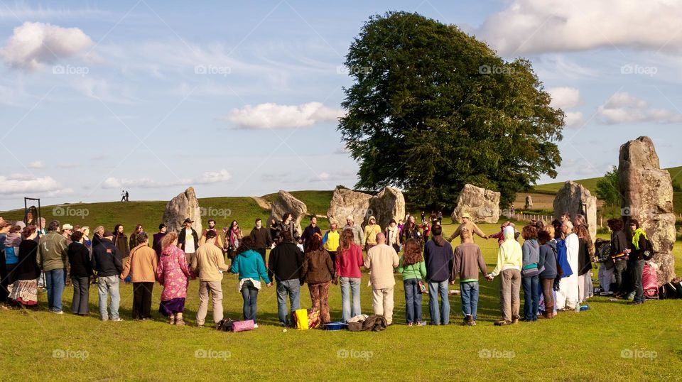 A group of people join hands in a moment of quiet reflection surrounded by ancient standing stones at Avebury, UK 