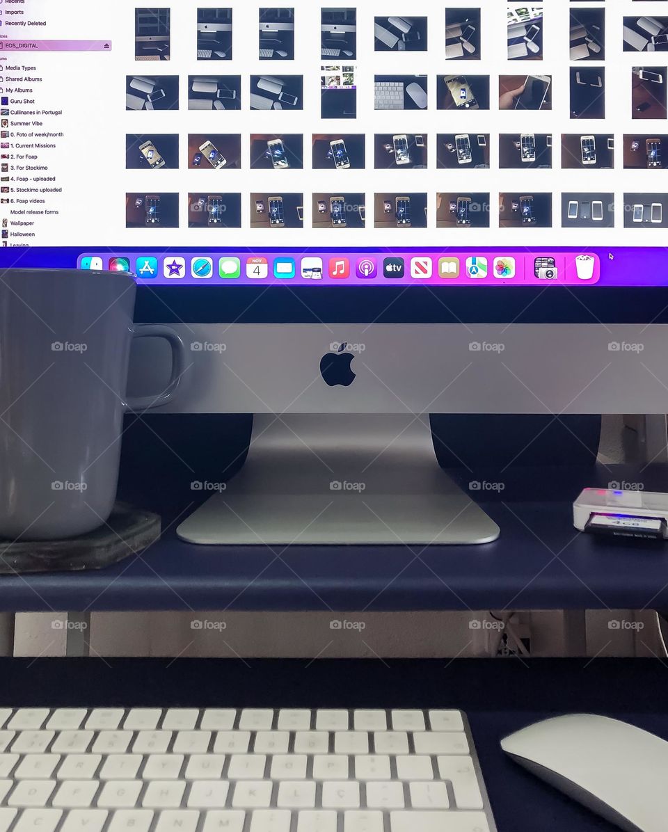 An iMac with iPhoto open on a purple desk with coffee mug, desktop and mouse, also a smart card plugged into a reader.