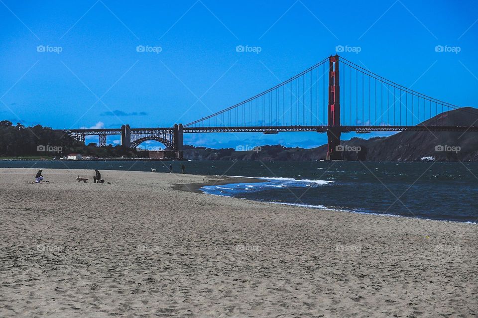 Looking down the beach at Crissy Field in San Francisco California at the Golden Gate Bridge on a warm sunny afternoon with clear blue skies, and you can see Fort Point in the distance