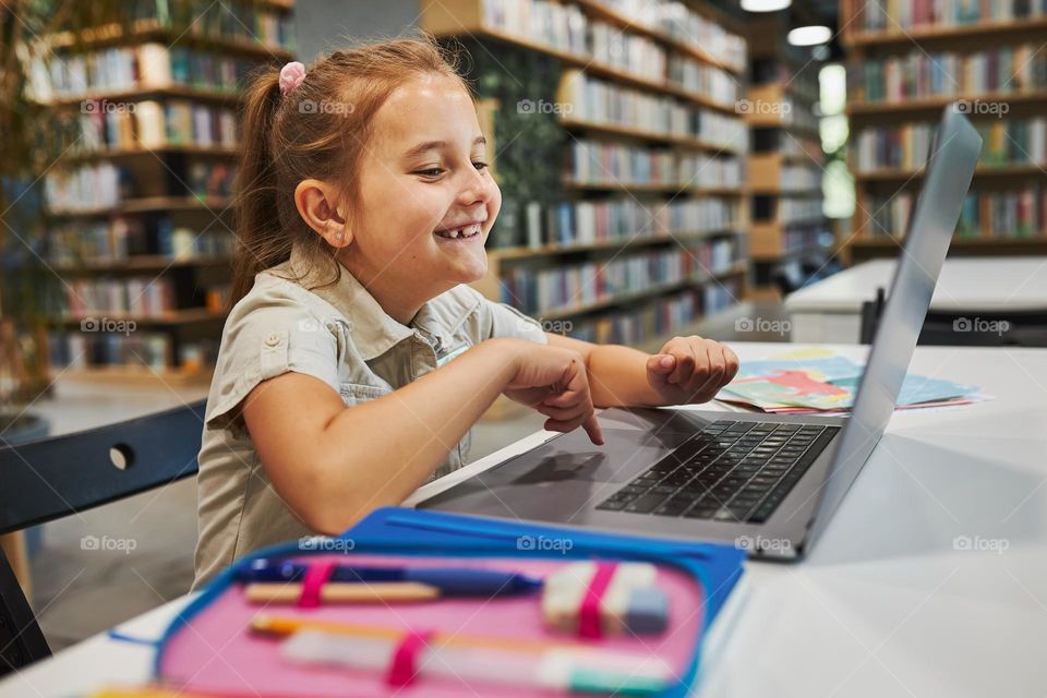 Cheerful student doing her homework using laptop in after school club at primary school. Back to school. Child using technology on elementary computer science class. Smart little girl learning from educational application at school