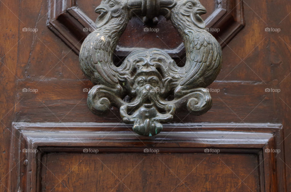 Close-up of metallic door knocker on wooden door of residential building in Florence, Italy.