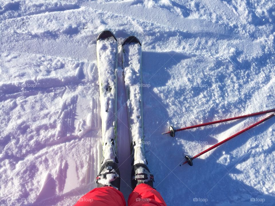 Looking down at feet wearing skis with ski poles beside