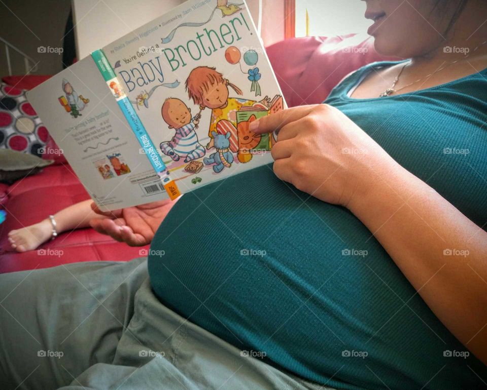 Mother reads to her toddler about her new baby brother