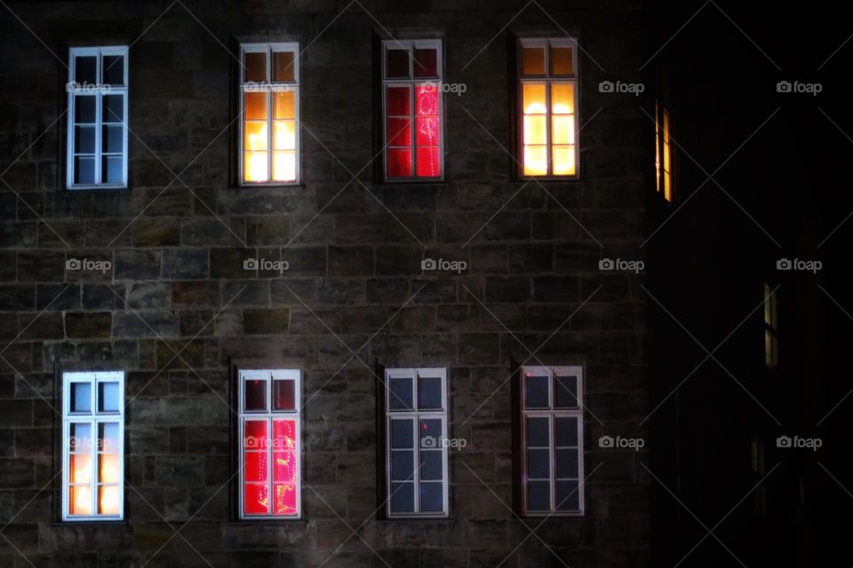 Red and gold illuminated lattice windows in a row in an old sandstone house in the dark