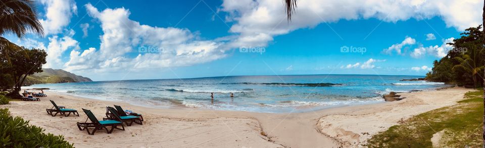 Stunning panoramic image of an unforgettable white sand beach being quenched by the cool blue ocean beneath tropical skies at its home surrounded by palm trees and welcoming tourists exploring the breathtaking beauty of the Caribbean islands 