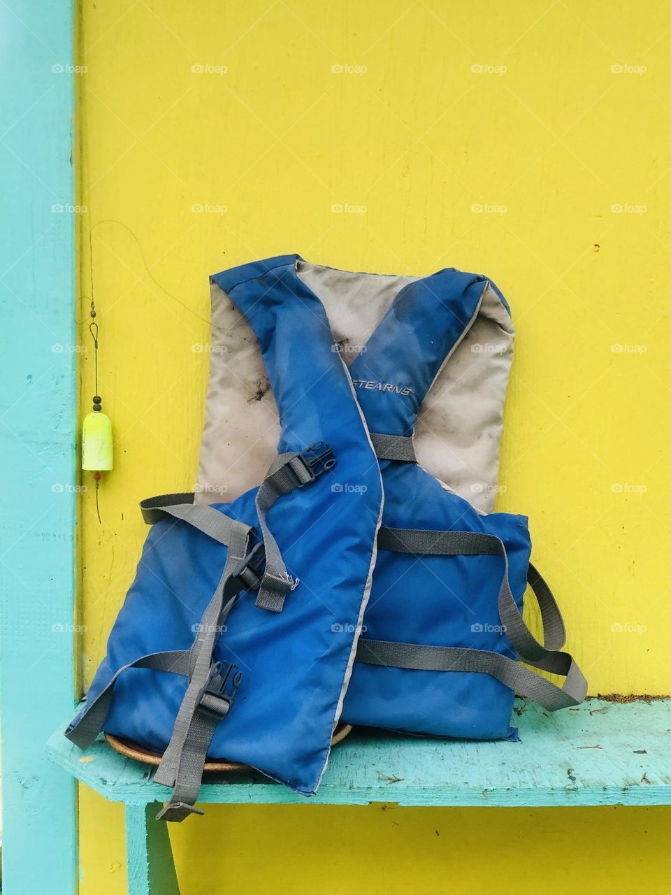 Still life of life preserver and fishing tackle against painted yellow shed. Equipment is ready for summer boating!
