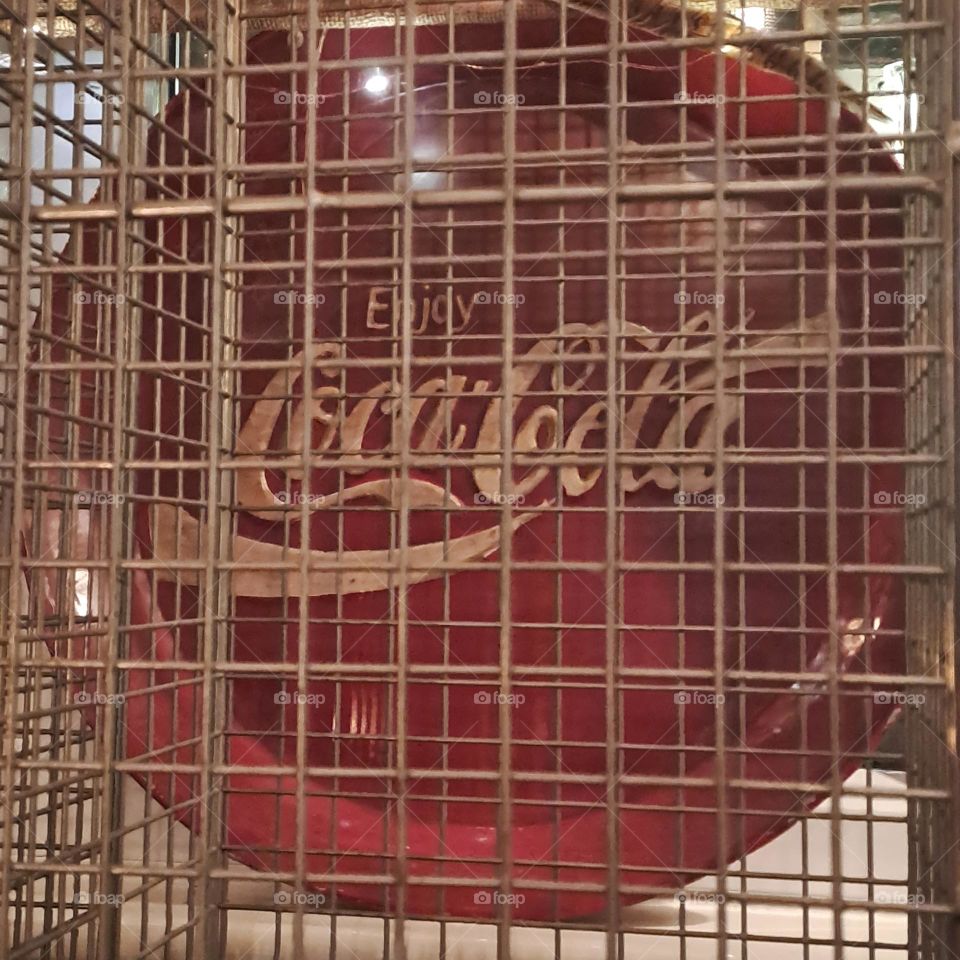 coca cola symbol on red tray behind a bronze wired cage display. advertising