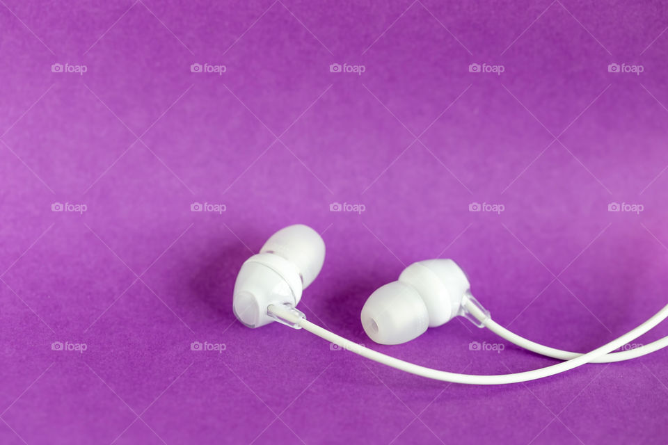 Pair of simple white earbuds on purple background