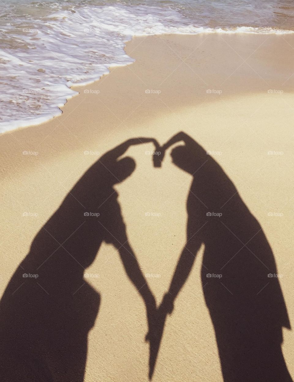 Couple on the beach makes a heart with their shadows, lesbian couple on the beach, LGBTQ couple on the beach, making shadow hearts with two people 