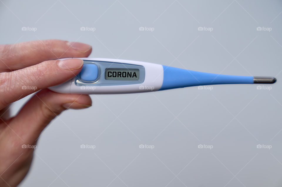 Female hand holds clinical thermometer with covid-19 text on the screen during global covid-19 or corona pandemic.