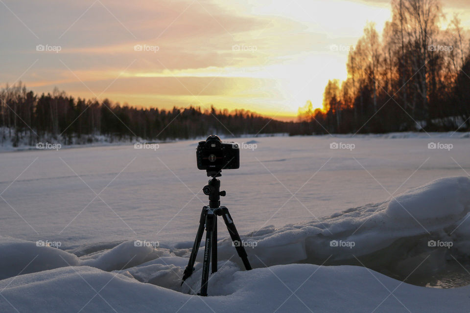 Photo of a camera taking a timelspse at sunset,  at frozen river