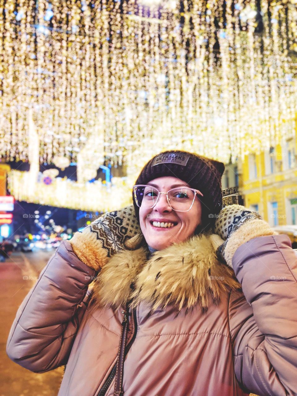 Portrait of young happy, beautiful woman in eye glasses in Christmas,  New Year city with illumination and garlands