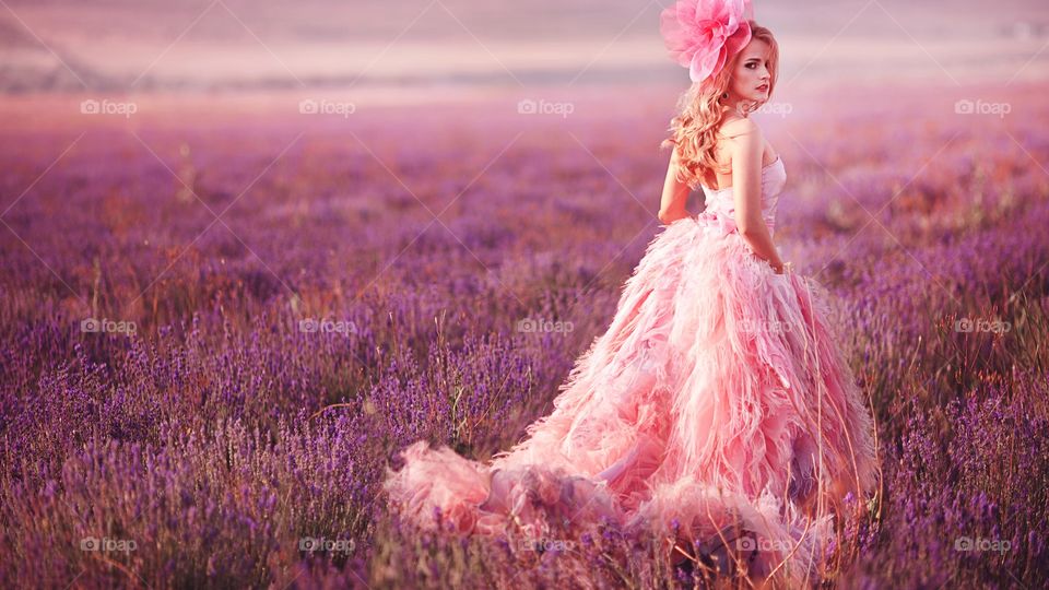 Blonde Hair Girl Model With Pink Dress Is Standing On  Lavender Field During A Photo Shoot .