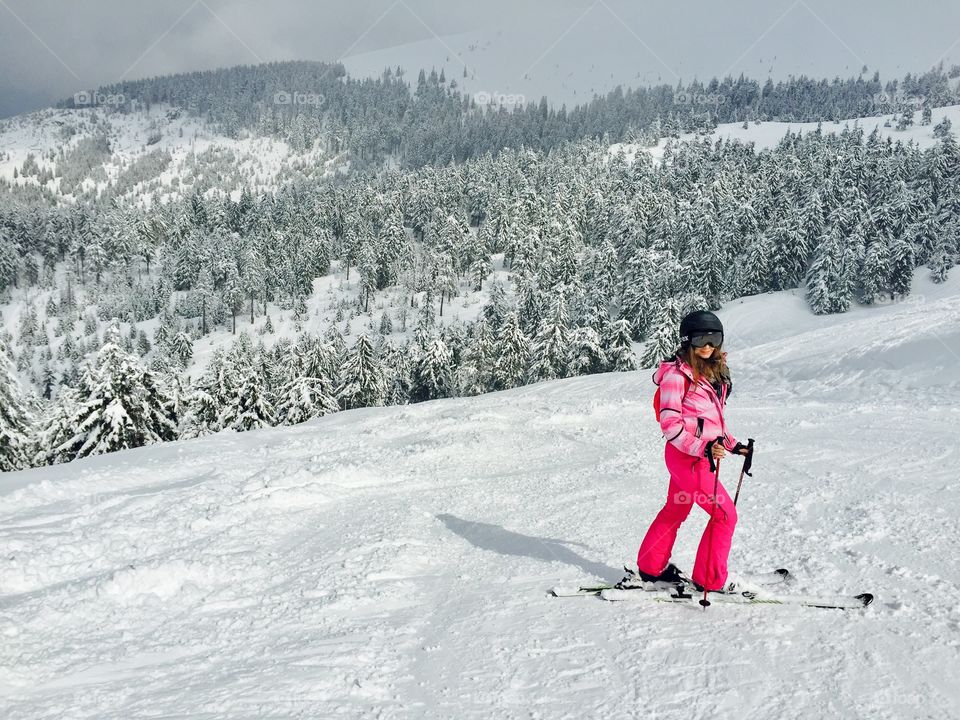Woman in pink ski costume surrounded by snowy evergreen forest