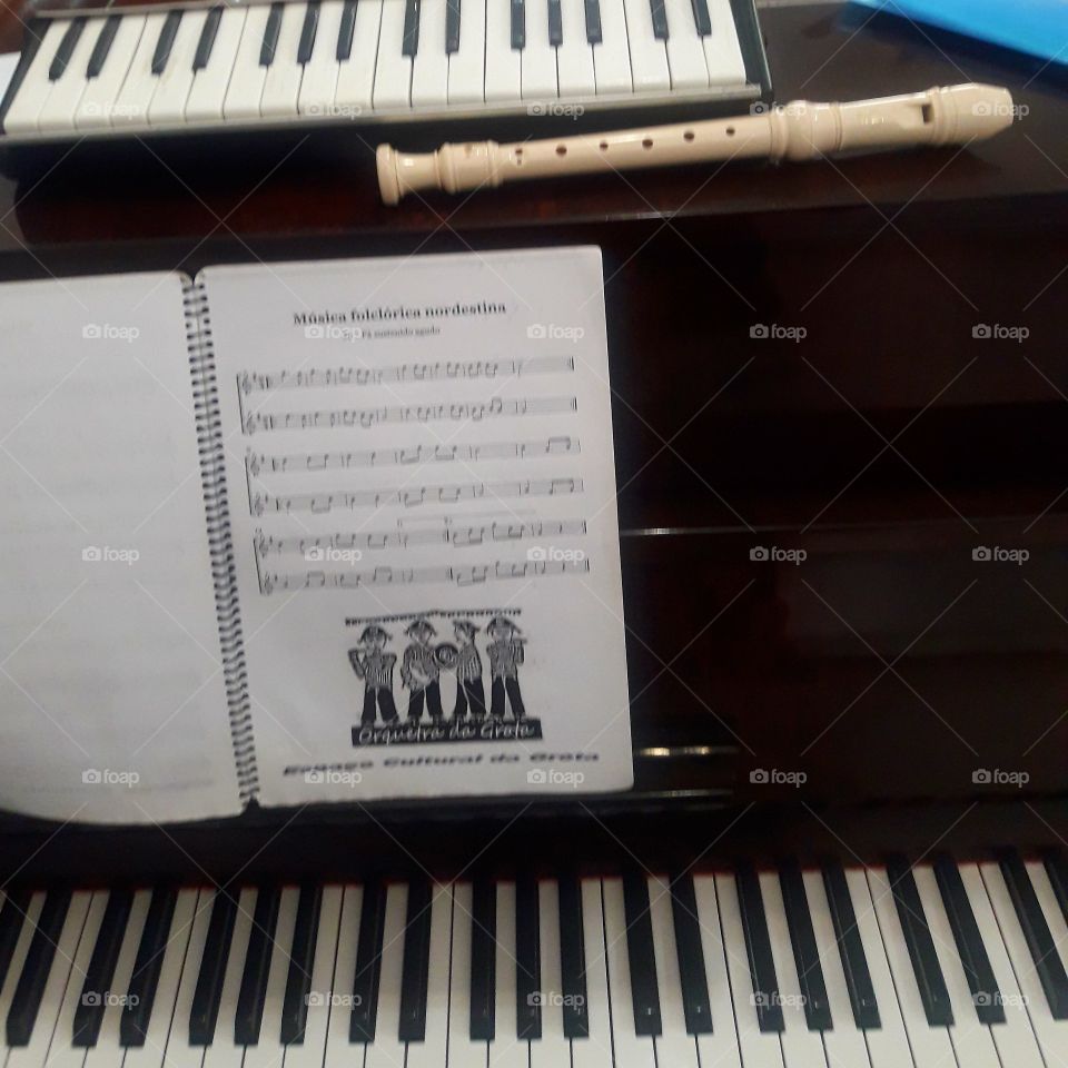 Um piano de armário, com uma partitura uma flauta doce  e uma escaleta.