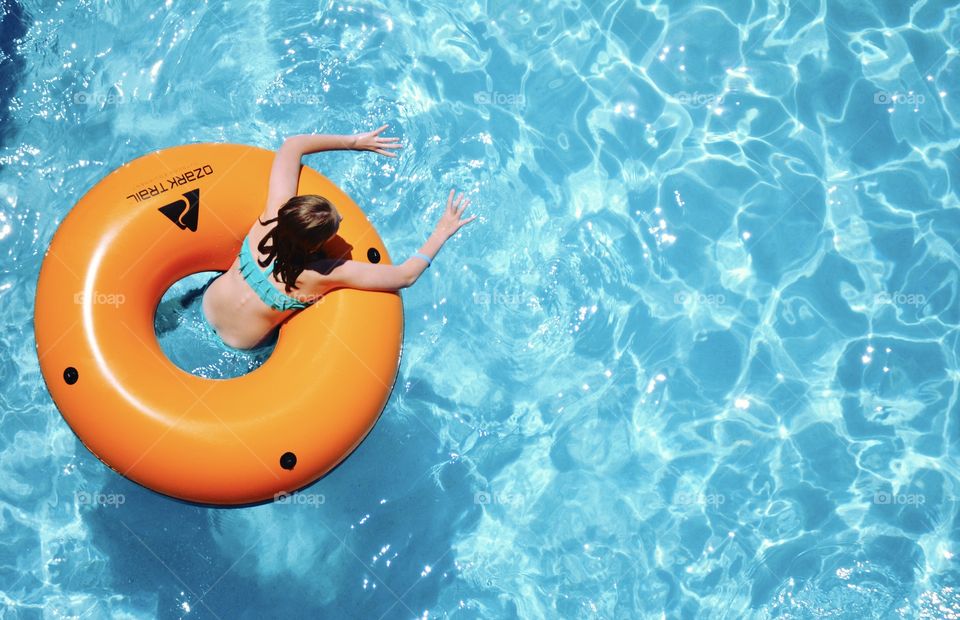 A young girl floating on a orange pool float. 
