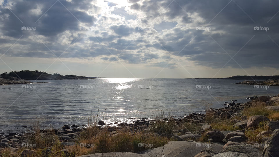 By the sea, sun shines through the clouds.
Vid havet, solen skiner genom molnen 