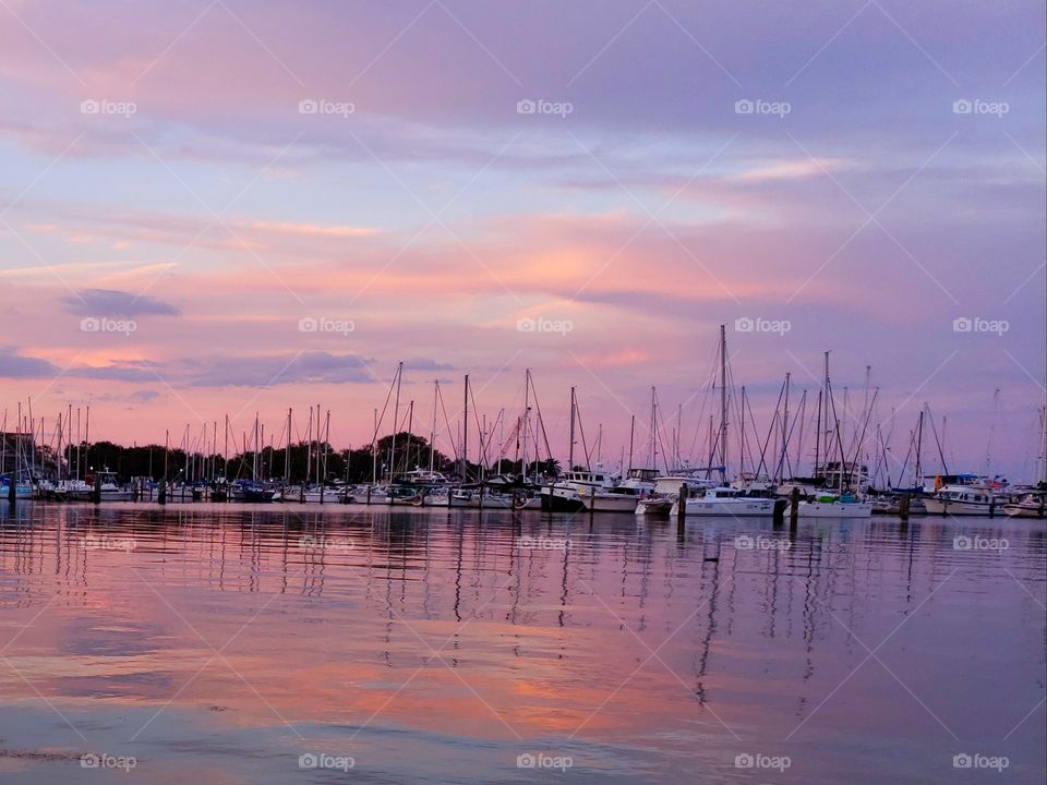 colorful sunset of oranges, pinks, blues, and purples in the sky over a marina full of small boats with the water reflecting the colors