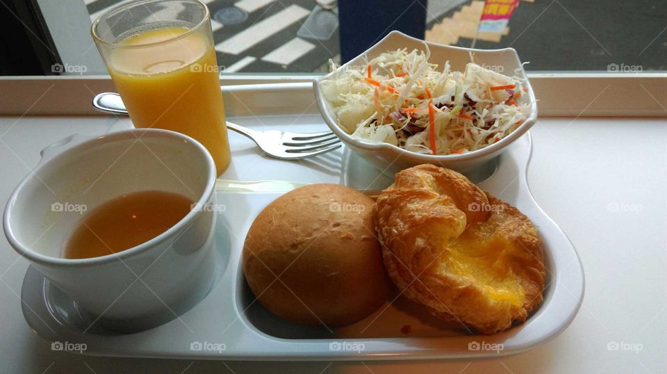 Special bread with salad and one glass of orange juice on the white tray for my breakfast.