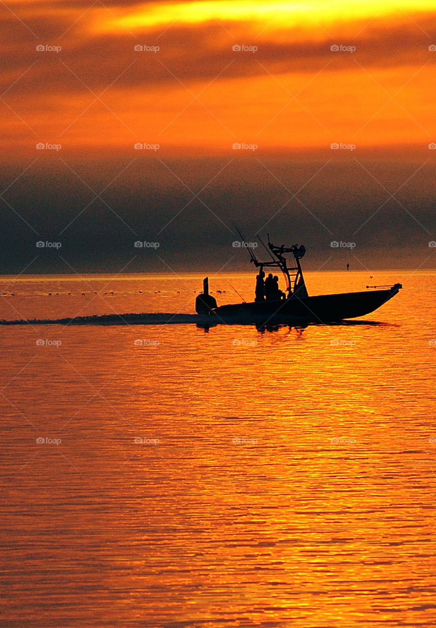 A silhouette of a boat with fishermen heads back to the shore through a magnificent orange sunset