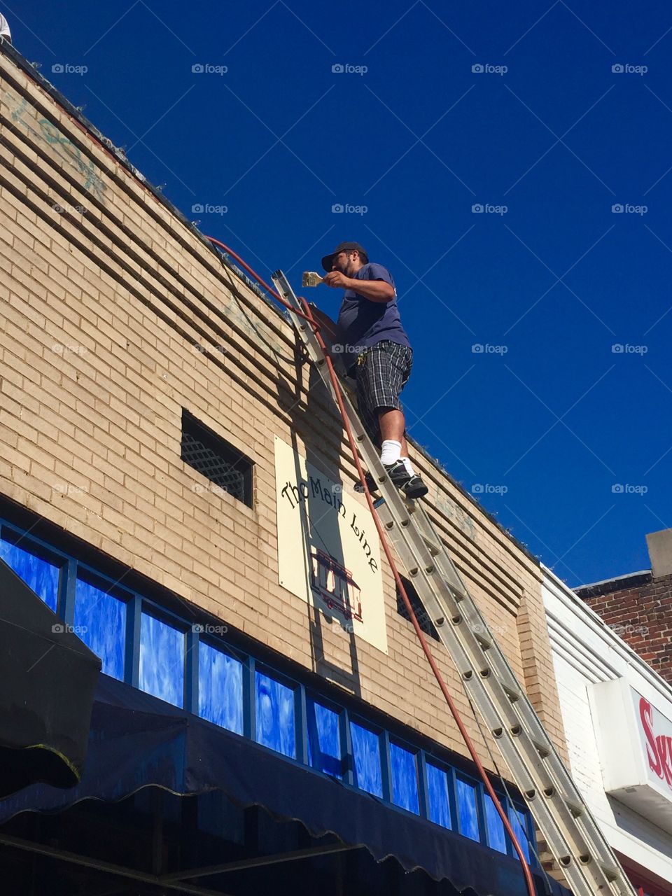 A painter painting the outside of a small business standing on a ladder