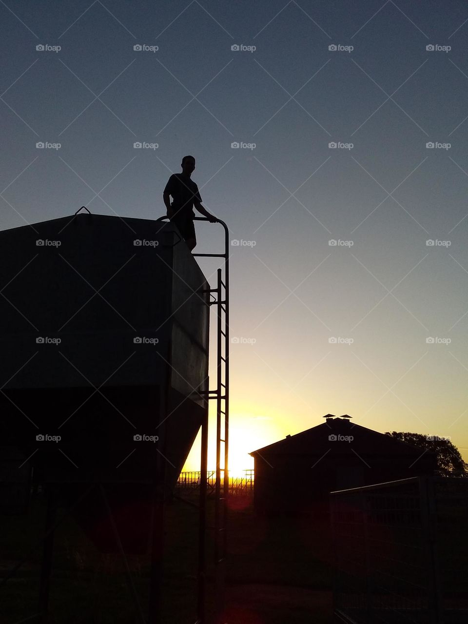 person on grain silo silhouetted against setting sun
