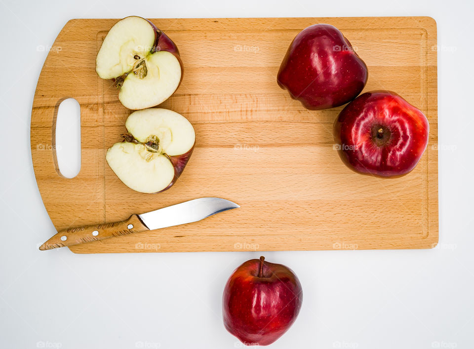 red apples lie on a wooden cutting board one apple cut in half and a knife lies nearby