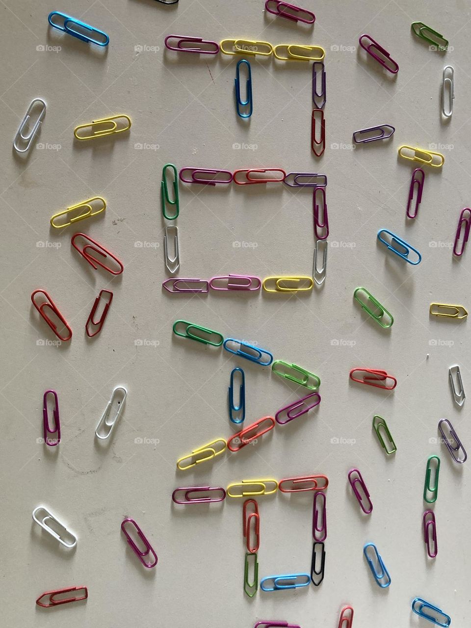 Na mesa branca com clipes está escrito FOAP, ao lado muitos clipes espalhadas dando charme a escrita.