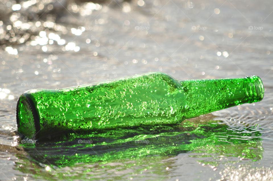 green glass bottle in the baltic sea water on the beach