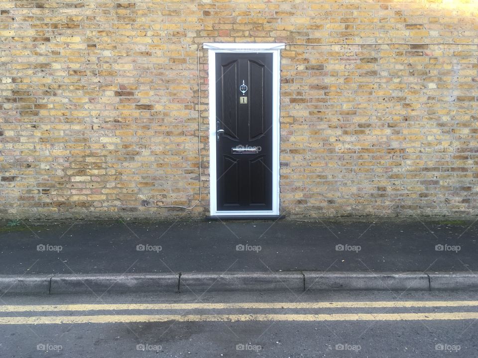 Entrance to 1 Cromer Road, Watford, Hertfordshire, in Winter. Black wooden door, knocker, letterbox, knob. Brick wall with no windows. 