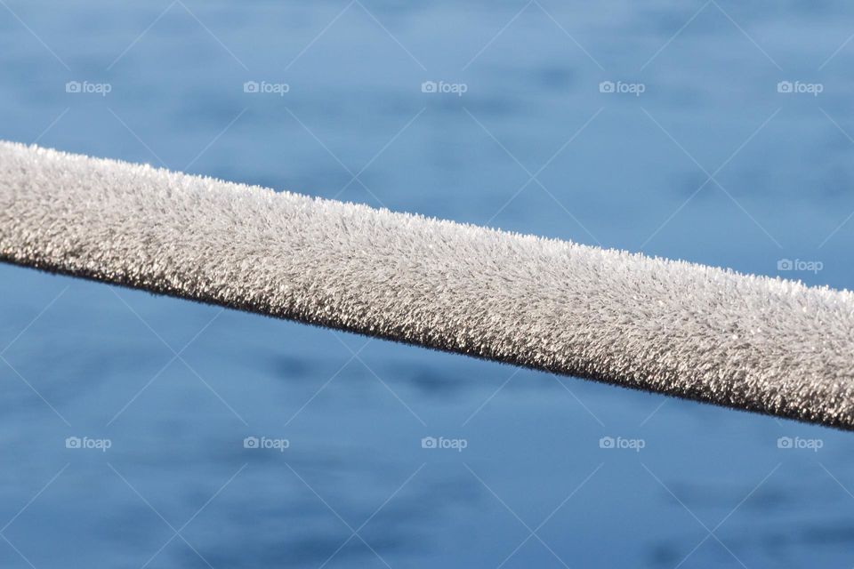 Metal railing covered with beautiful frost on a cold winter day, frozen blue lake in the background 