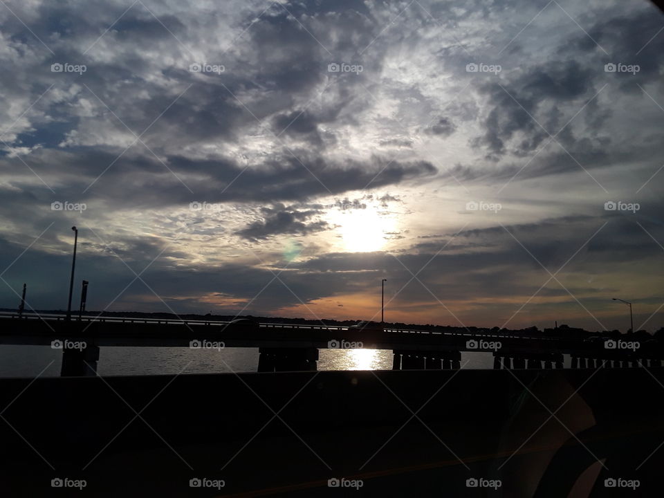 Cloudy sunset w/ a bridge silhouette in the forefront.