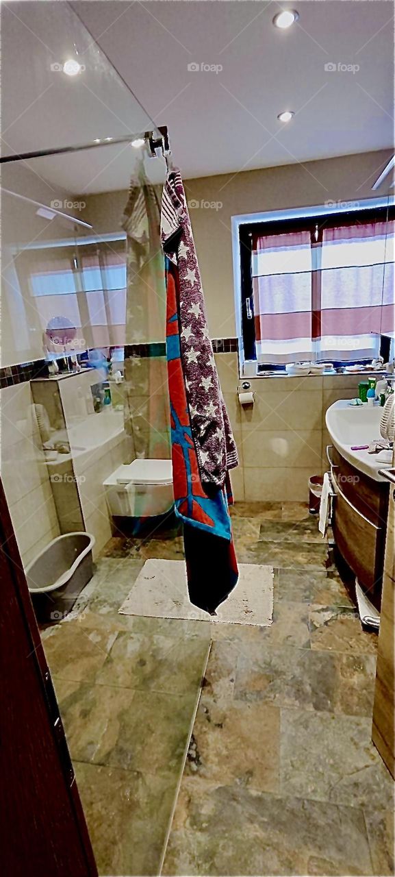 This is the glass encased shower with bathtub in the beautiful house in “Bavaria”, Germany. A sink with a makeup table for toiletries, a hairdryer et cetera is on the right by the window. 2023. Hypnotic Productions