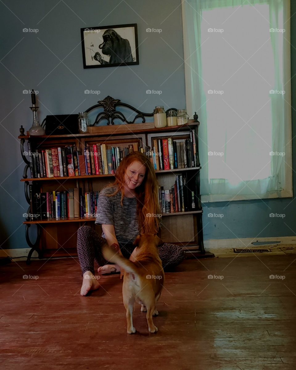 Red haired girl playing with small brown dog in a library space