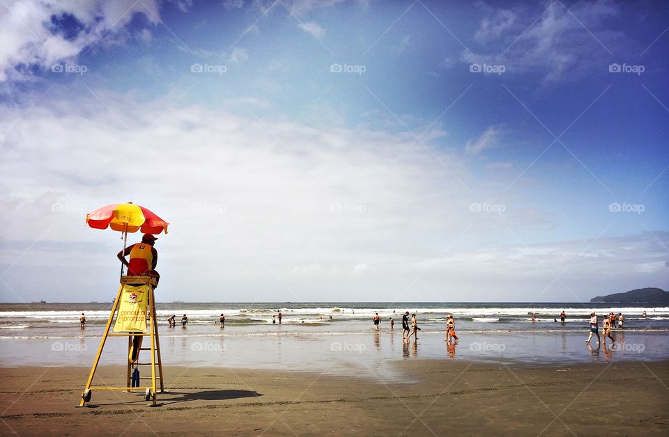 Lifeguard observes people walking on the beach from the top of his chair