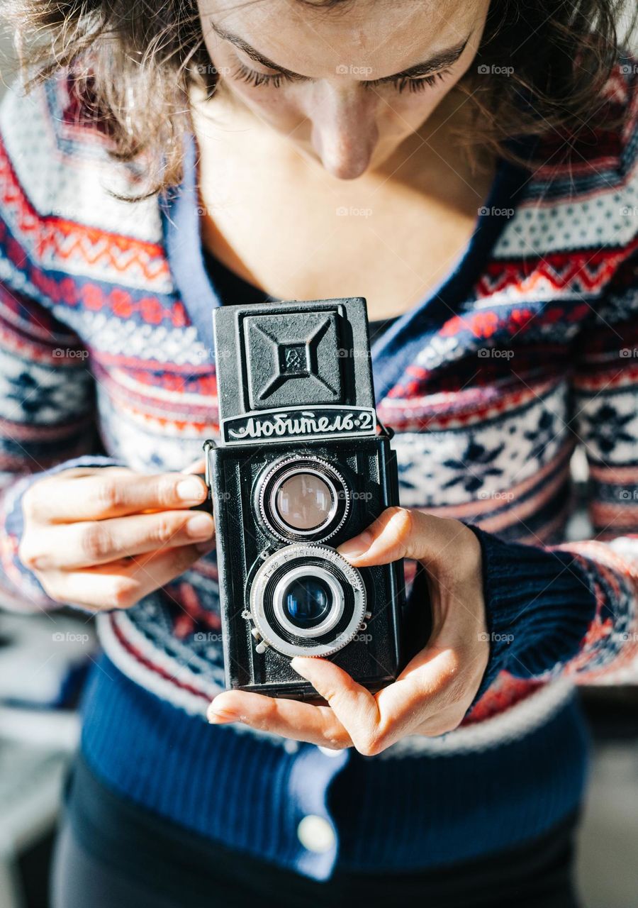 Woman holding a vintage film camera, while being in her photo studio, on a sunny day.