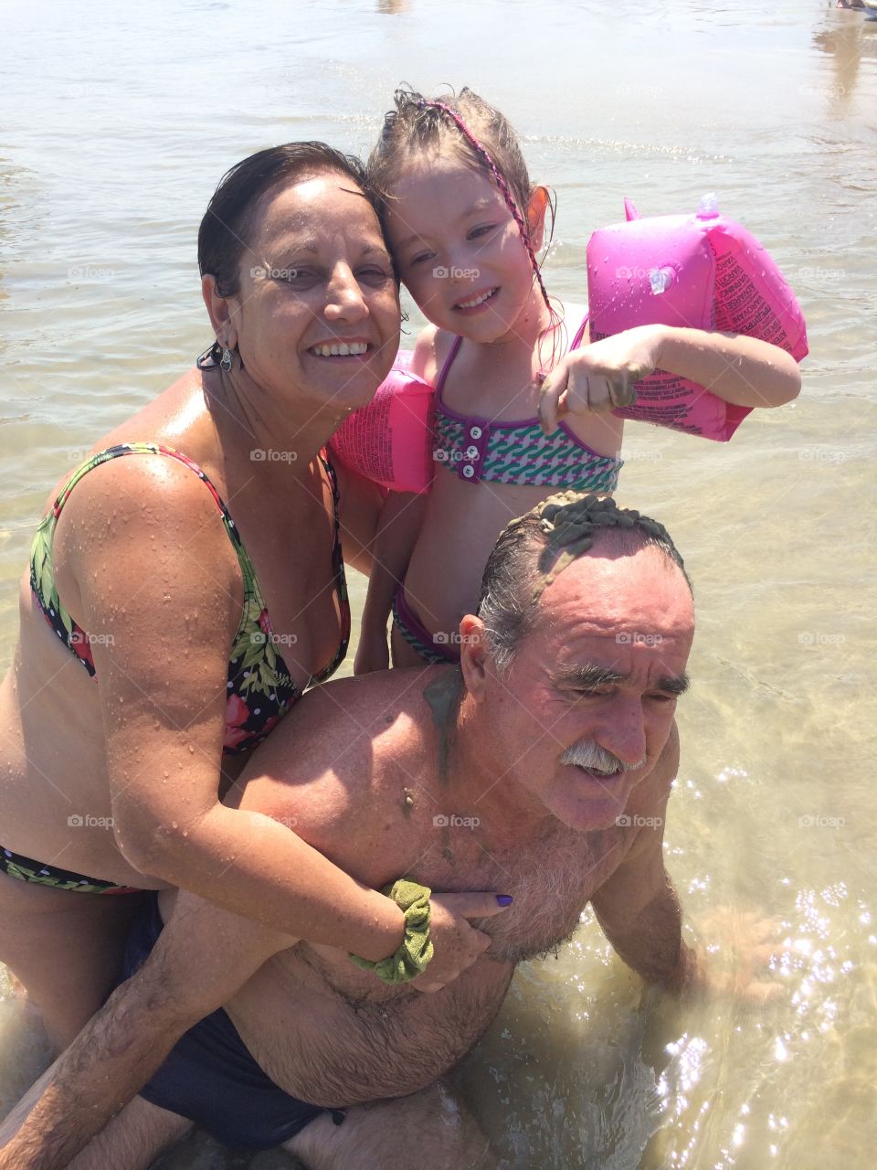 A alegria do vovô e da vovó brincando com a netinha na Praia. Vira a areia e a água do mar. 