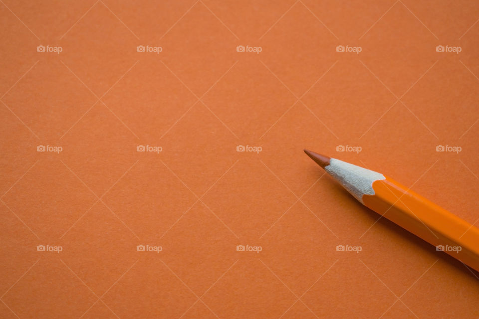 Orange pencil on orange paper background