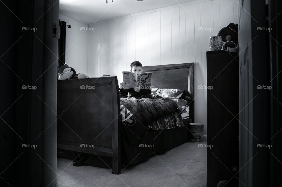 Boy reading story book sitting on bed