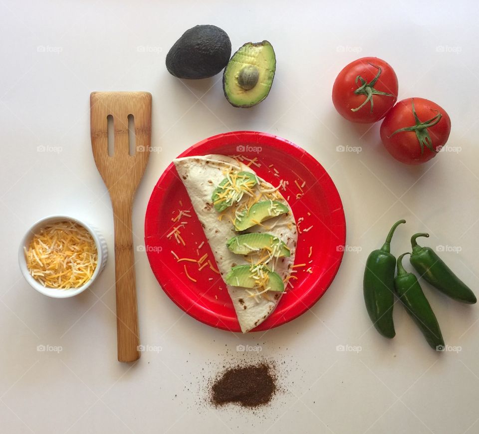Homemade burrito on red plate with wooden spatula and ingredients. 