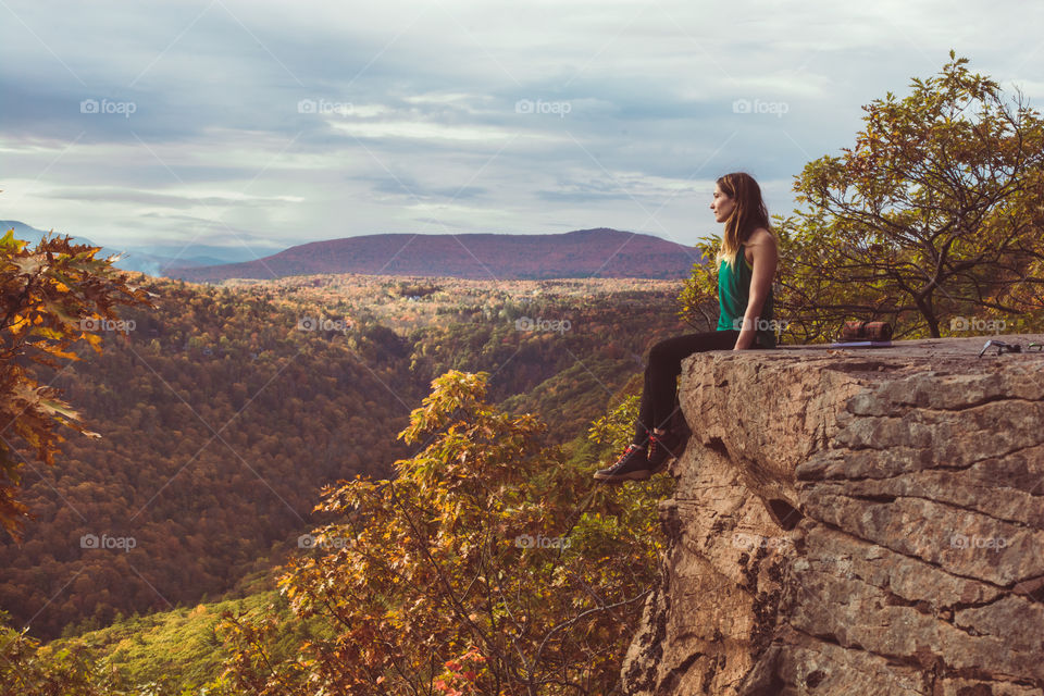 A young woman hiker looks out at the mountain range of a forest upstate New York in the Catskills mountains 