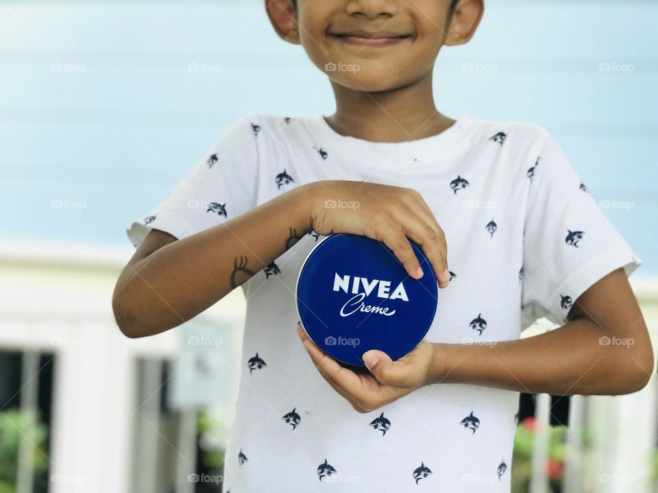 A boy holding Nivea cream with his both hands and smiling.