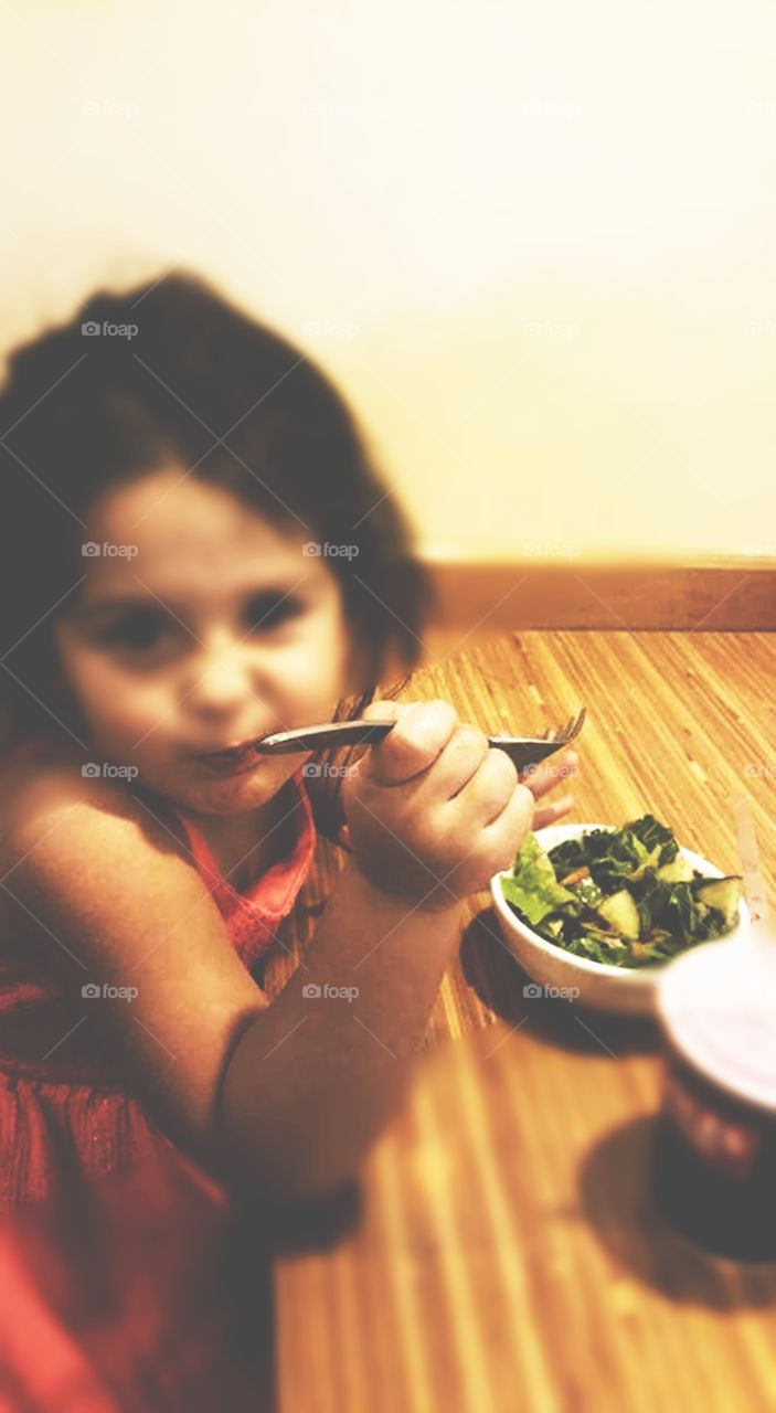 Blurred image of little girl, enjoying a crisp green salad.