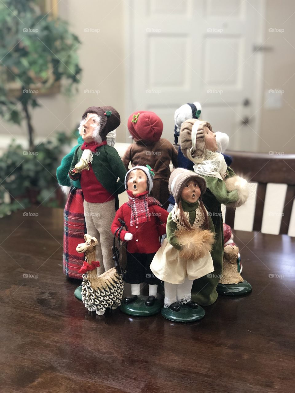 Diverse group of Christmas carolers on wood table indoors with plants and door in background 