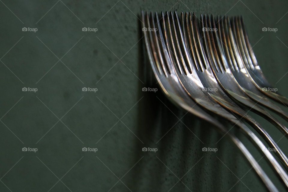 Close up of silver forks standing on green wall 